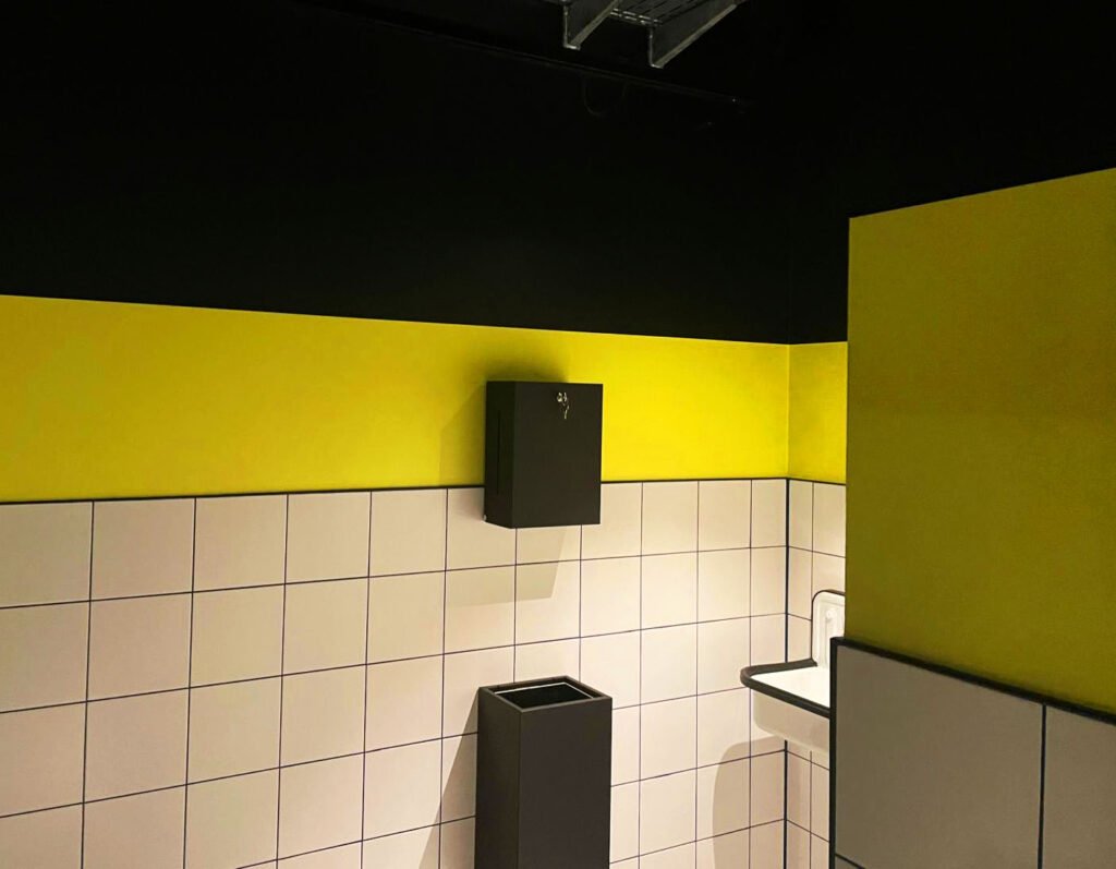 Wand mit weißen Fliesen, darüber ist die Wand gelb und schwarz gestrichen