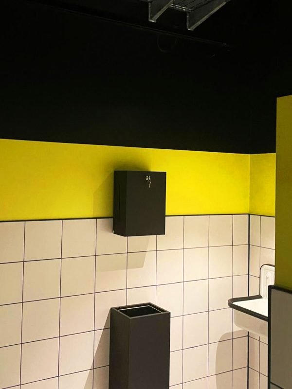 Wand mit weißen Fliesen, darüber ist die Wand gelb und schwarz gestrichen